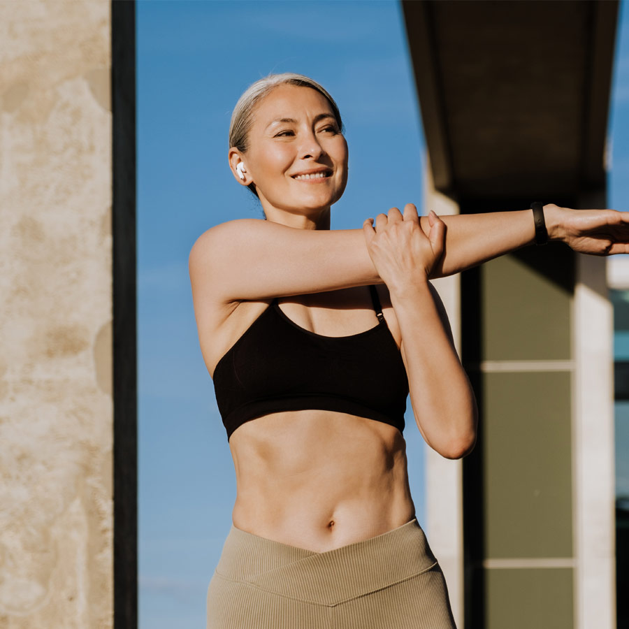 Asian mature woman in earphones doing exercise during workout outdoors