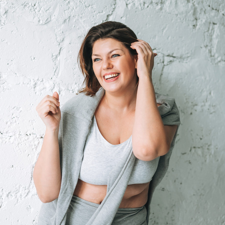Beautiful happy emotional brunette young woman plus size body positive in comfortable sport wear near white brick wall
