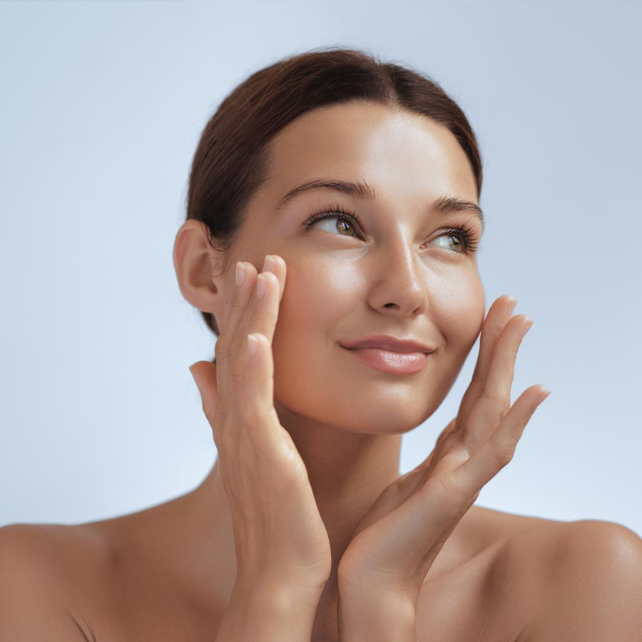 Skincare. Woman with beautiful face touching healthy facial skin. Beautiful portrait of smiling Asian girl model with natural makeup enjoys glowing hydrated skin on blue background closeup.